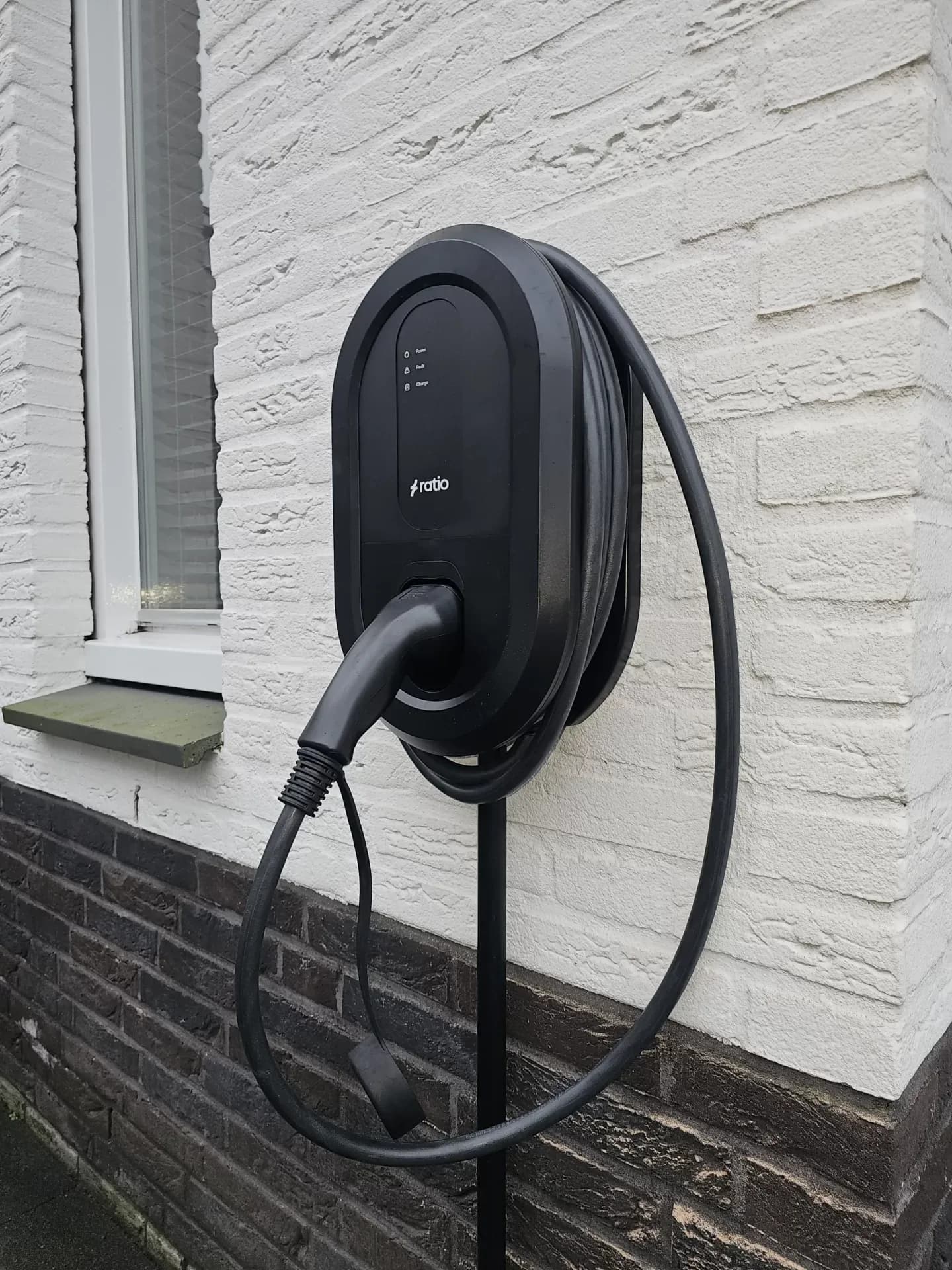 Opgeleverd laadstation tegen een woning, met de laadkabel opgerold